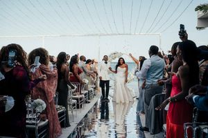 Wedding guests stand in line outdoors at a reception venue during a daytime celebration.