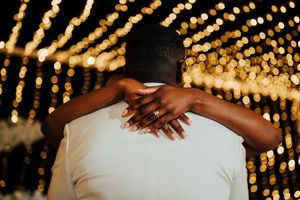 Two people embrace in a romantic moment against a backdrop of glowing string lights creating a magical bokeh effect.