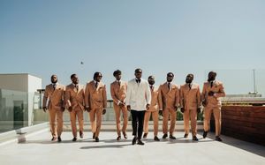 A group wearing matching orange jumpsuits stands in a line on a rooftop with one person in white in the middle.