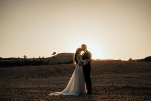 Silhouetted wedding couple embraces during golden hour sunset in open field.