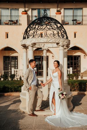 A romantic wedding couple shares intimate moments in a Mediterranean-style courtyard with arched architecture and warm lighting.