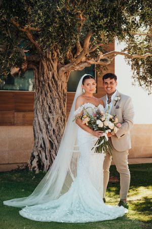 A wedding couple poses in front of a majestic old olive tree on a sunny afternoon.