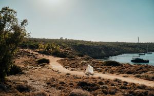 A panoramic coastal landscape view showing rugged cliffs, blue waters and arid terrain under a clear sky.