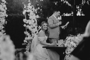 A black and white wedding reception photo showing guests and decor with white floral arrangements.