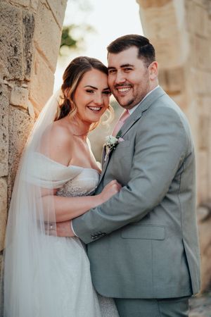 A romantic wedding couple shares intimate moments in a stone archway while wearing a white gown and gray suit.