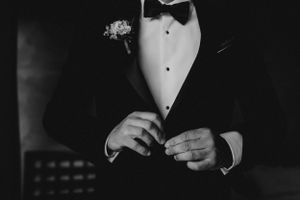 Close up of groom in black tuxedo adjusting bowtie.