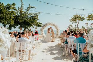 A panoramic view of an outdoor wedding ceremony setup with white chairs and floral arch under string lights.
