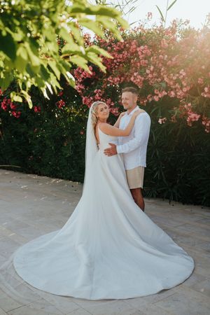 A romantic wedding couple dances together against a backdrop of pink flowering bushes at sunset.