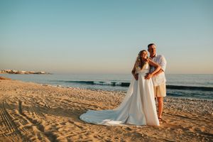 A romantic beach wedding photoshoot at sunset with couple walking along sandy shoreline and ocean waves.