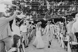 Wedding guests form a tunnel with raised arms as a couple walks through during an outdoor celebration in black and white.