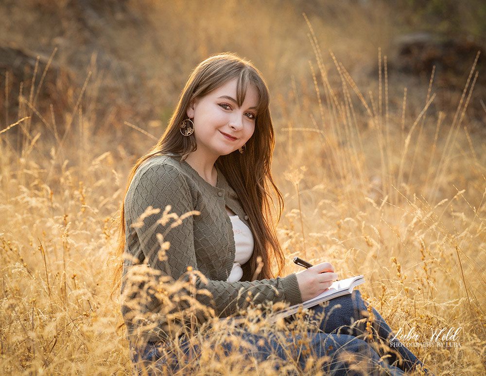 high school senior girl sitting on a hill in Post Falls outdoor studio dreaming or drawing photographer luba wold