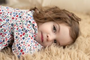 Sweet child wearing floral print dress lying on soft beige fur rug.