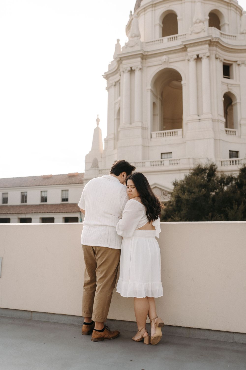 Romantic couple embraces while overlooking beautiful white Spanish colonial church tower at sunset.