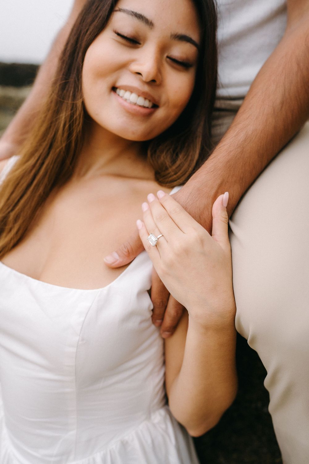 A person wearing a white dress shows off an engagement ring while smiling and looking down in a series of photos.