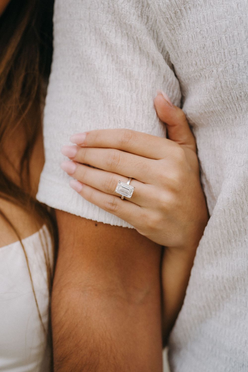 Close-up of an engagement ring on a hand against white fabric.