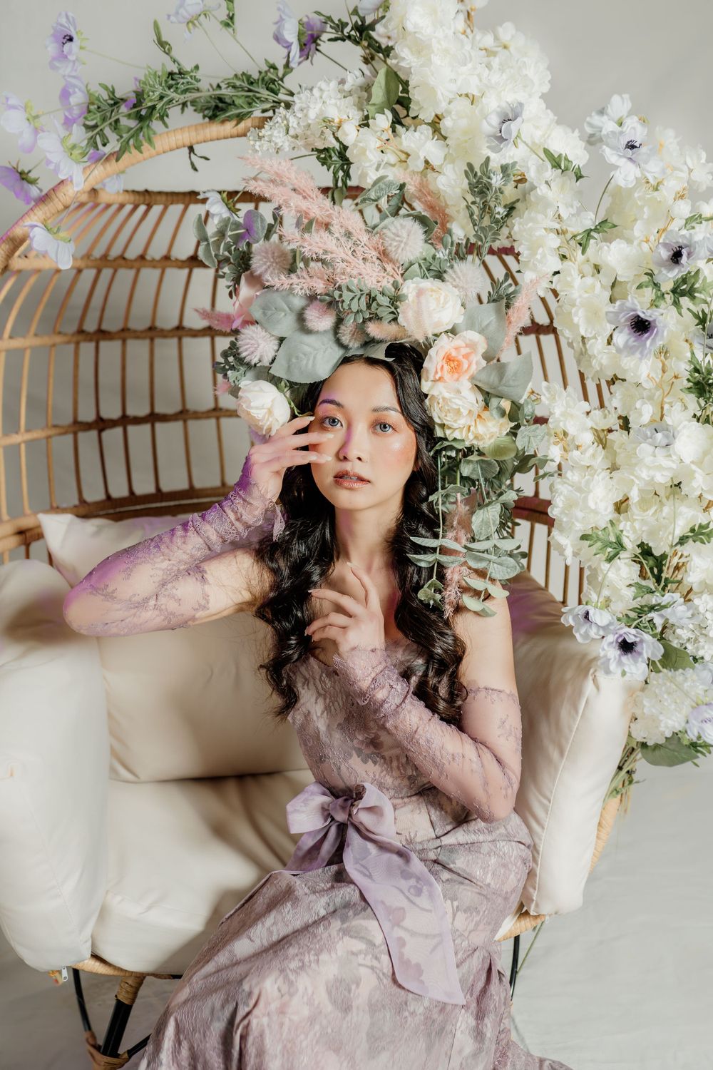 Romantic spring portrait in rattan chair with delicate lace dress and floral arrangement of white blossoms overhead.