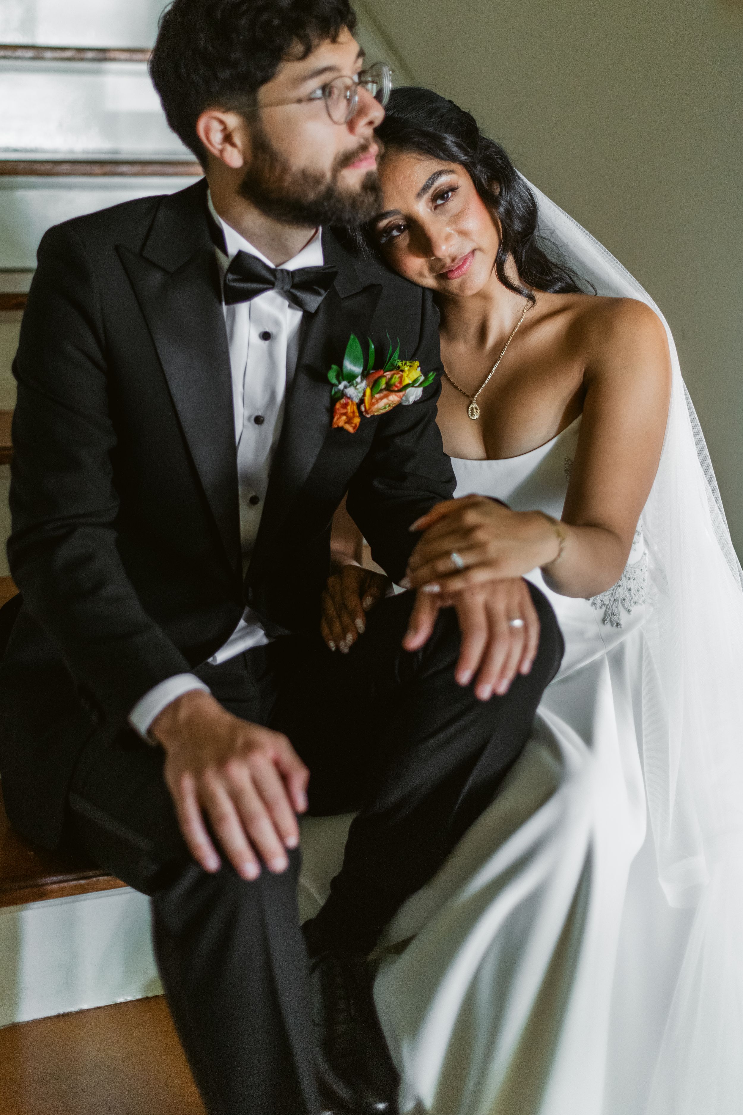 A romantic wedding portrait of a couple sitting together on stairs, with the groom in a tuxedo and bride in white dress.
