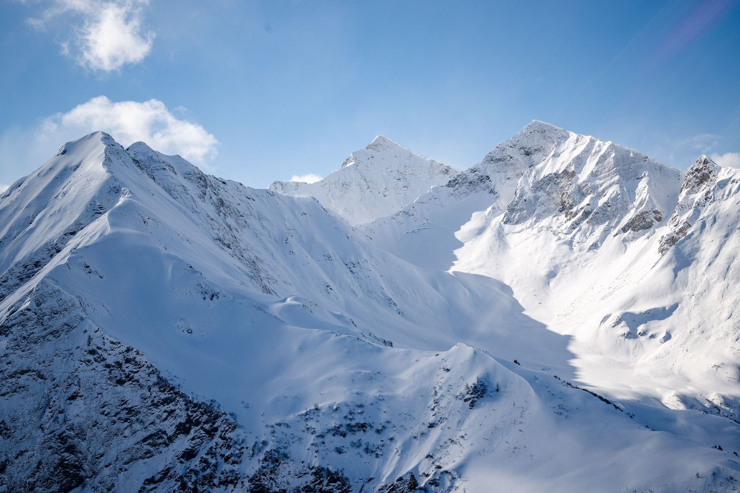 Majestic snow-capped mountain peaks rise against a bright blue sky in a pristine winter alpine landscape.