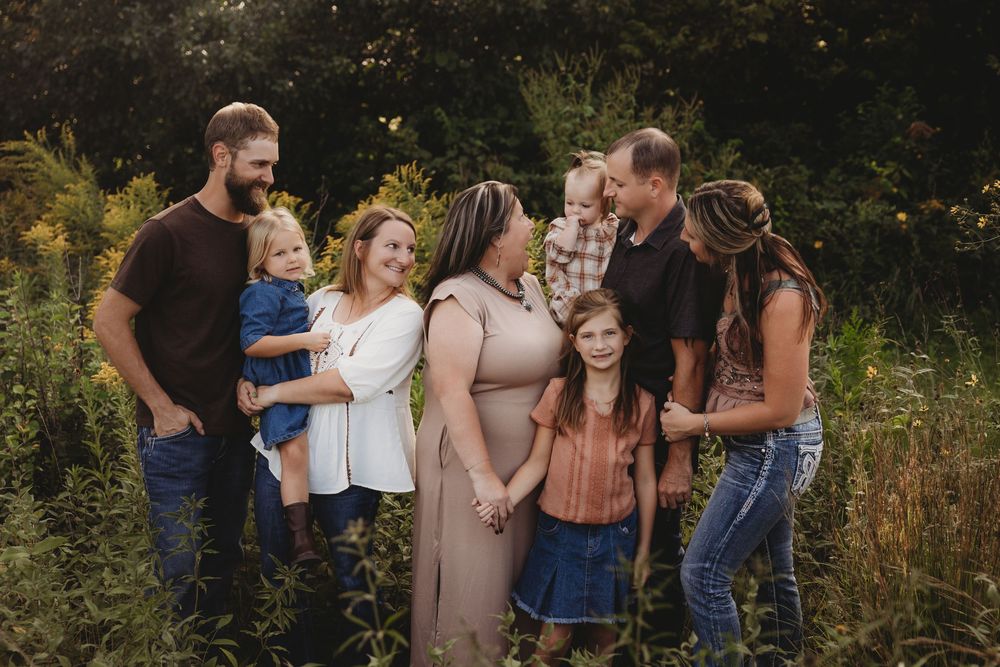 Family group portrait outdoors in a meadow, featuring adults and children smiling together in warm golden light.