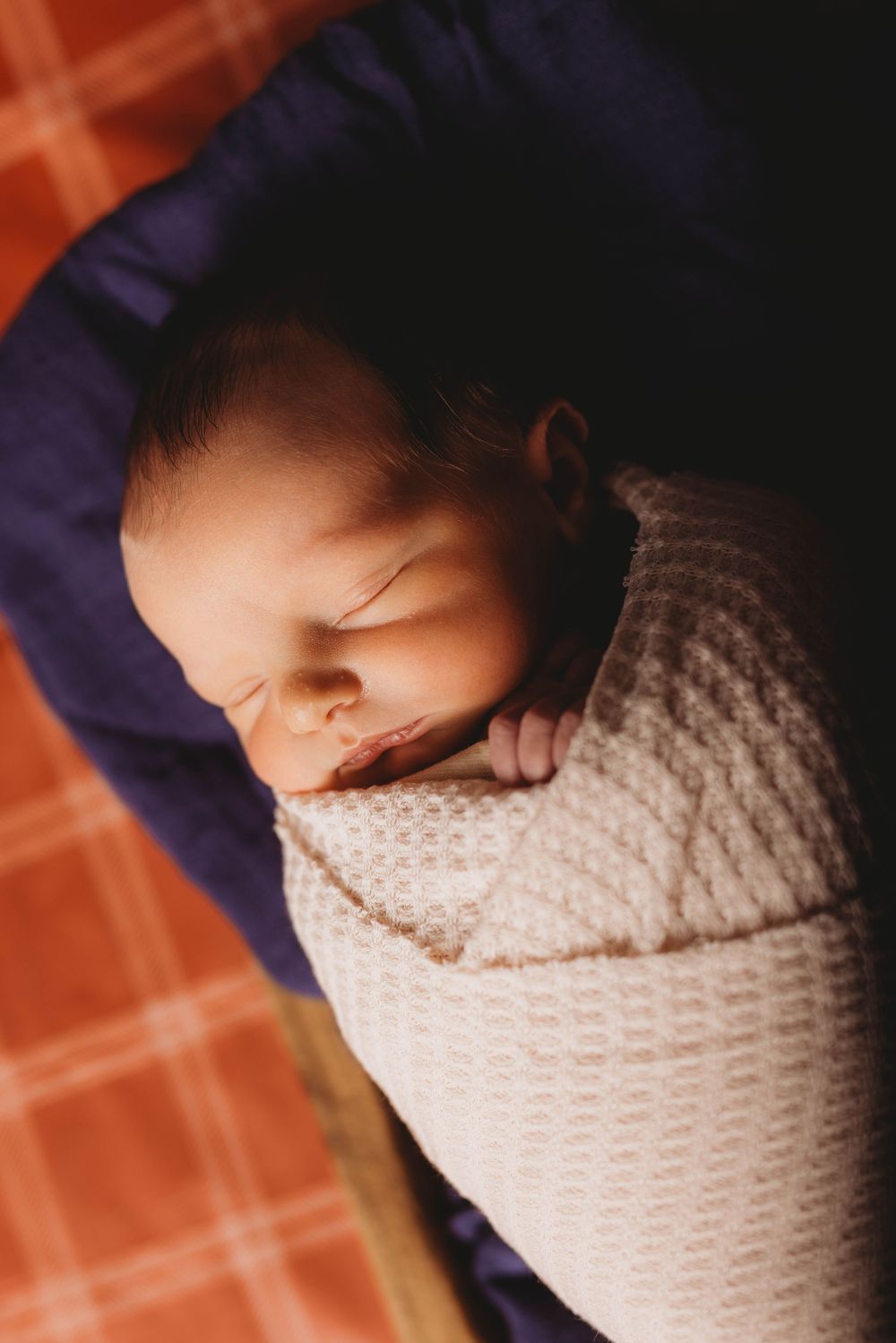 Sleeping newborn wrapped in knitted blanket with warm lighting.
