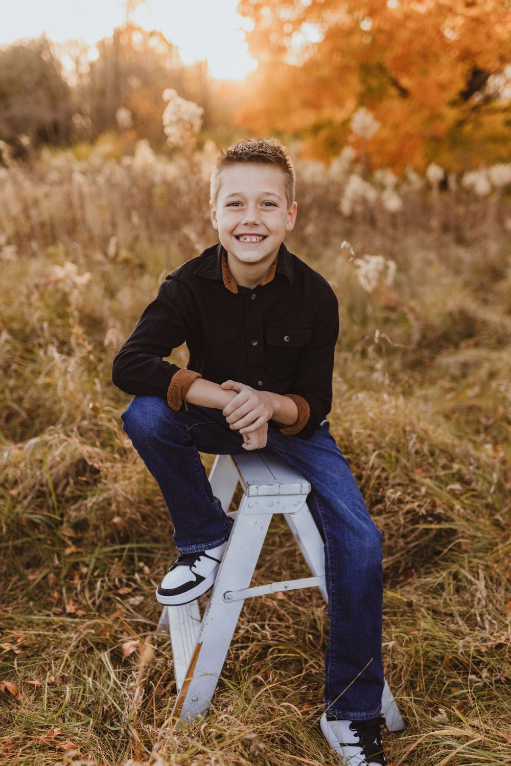 Young person sitting on white chair in autumn field with golden light.