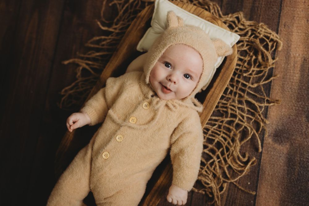 Infant wearing cream colored outfit on wooden background with straw accents.