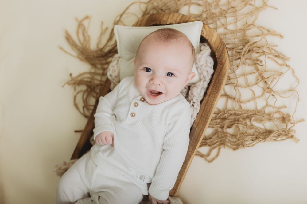 Baby in white outfit lying on textured beige backdrop.