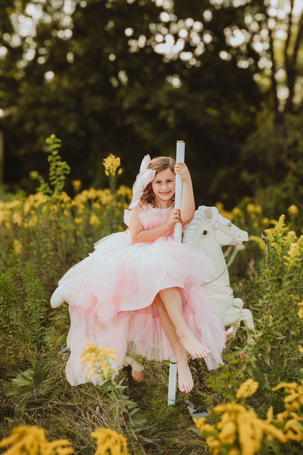 Young girl in pink tulle dress rides carousel horse in yellow wildflower field.