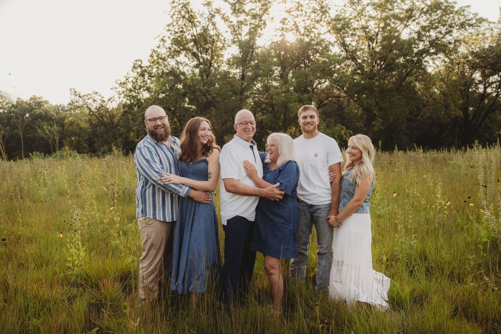 Family of six posing together in a lush green meadow during golden hour sunset photography session.