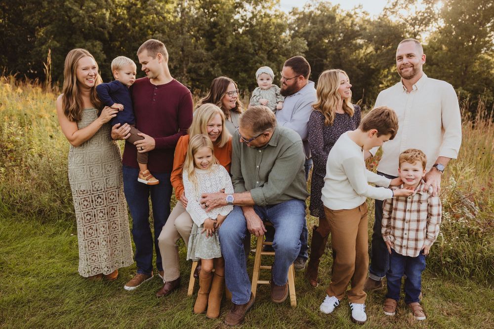 A large family poses together in a golden field during an outdoor fall photo session with children and adults.