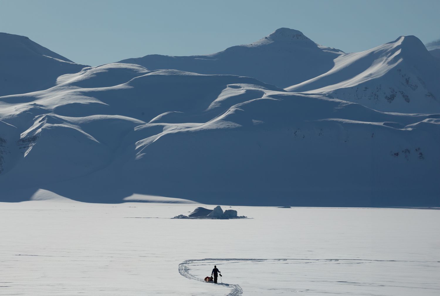 Minimalist winter landscape with lone figure skiing across vast snowy terrain.