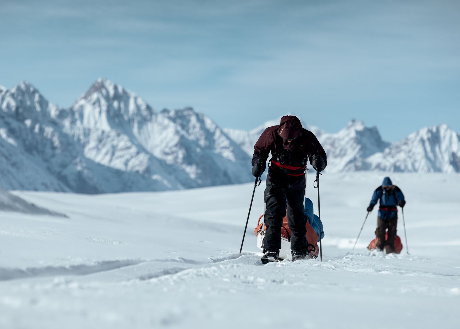 Skiers traverse across vast snowy mountain landscape under blue sky.
