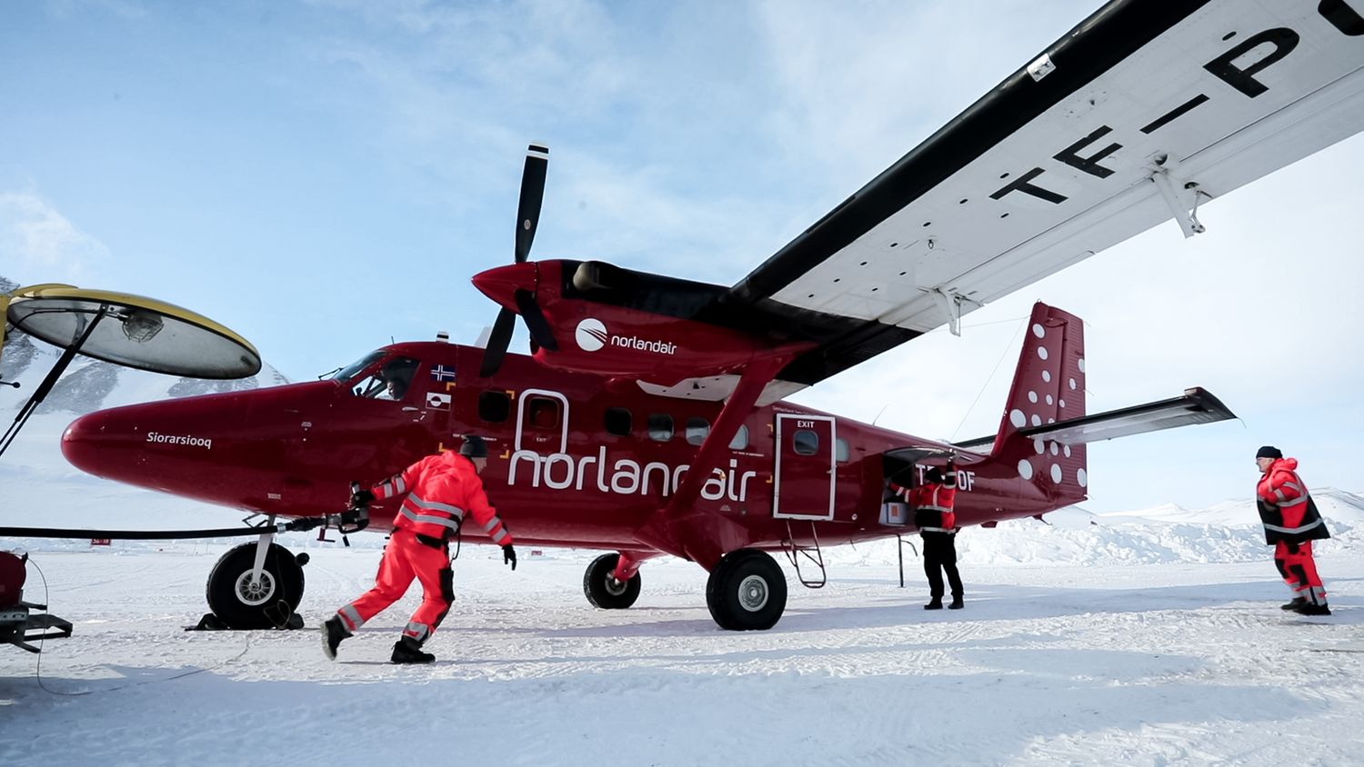 Red and white aircraft lined up on snowy terrain with mountains in background.