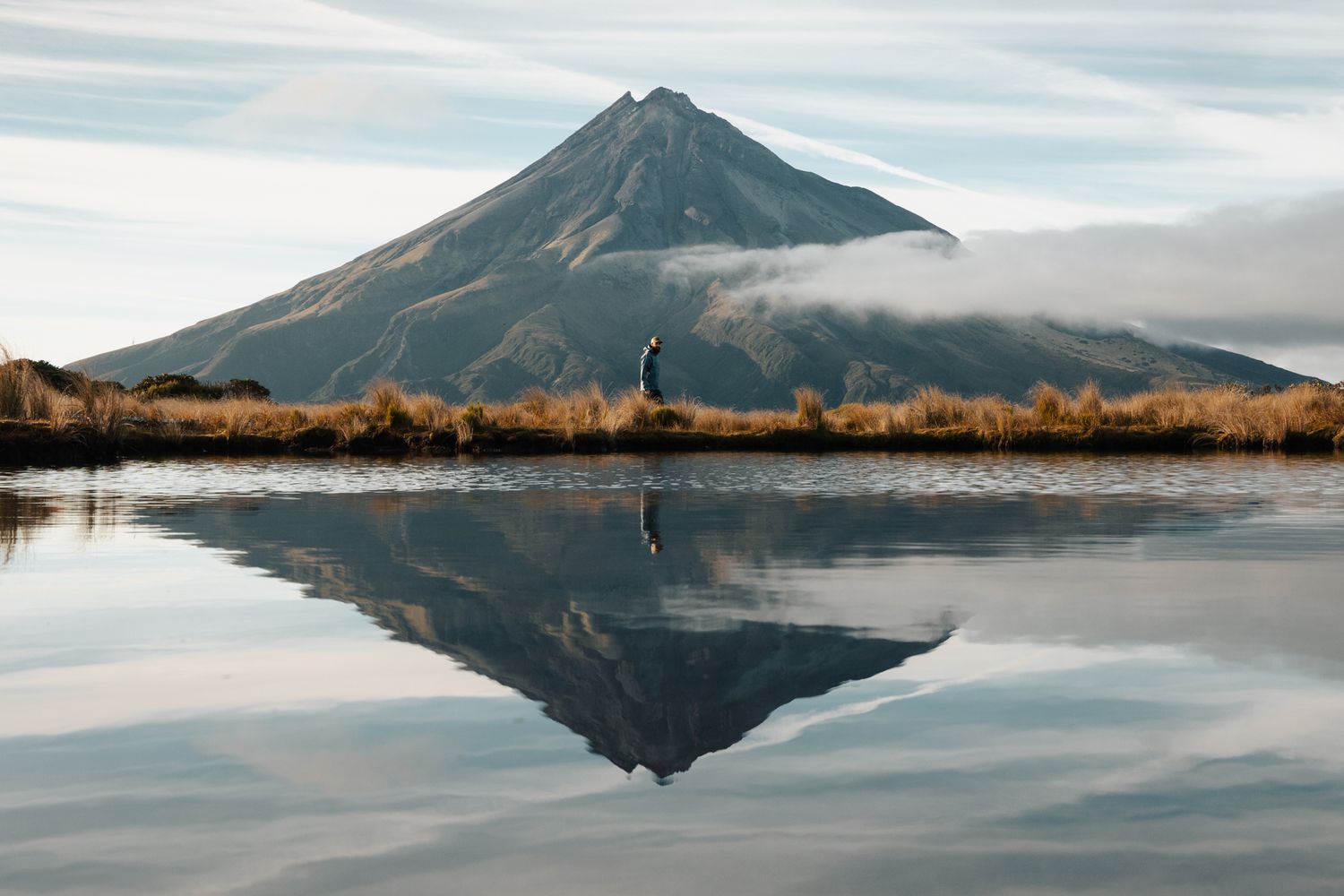 Mirror-like lake reflects a majestic mountain peak against a calm sky.