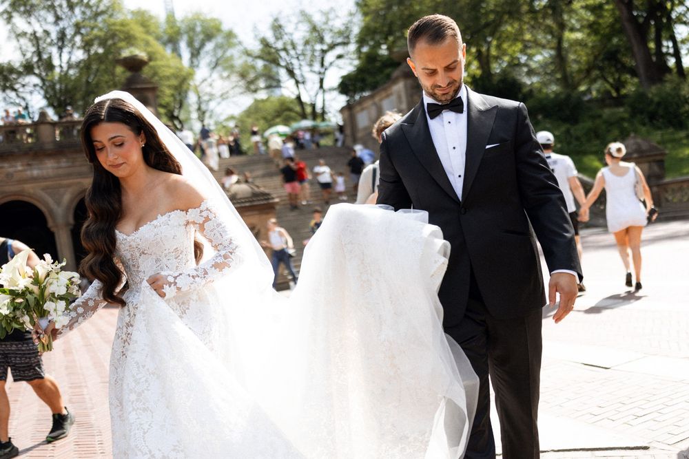 A couple walks along a brick pathway during their wedding photoshoot on a sunny day.
