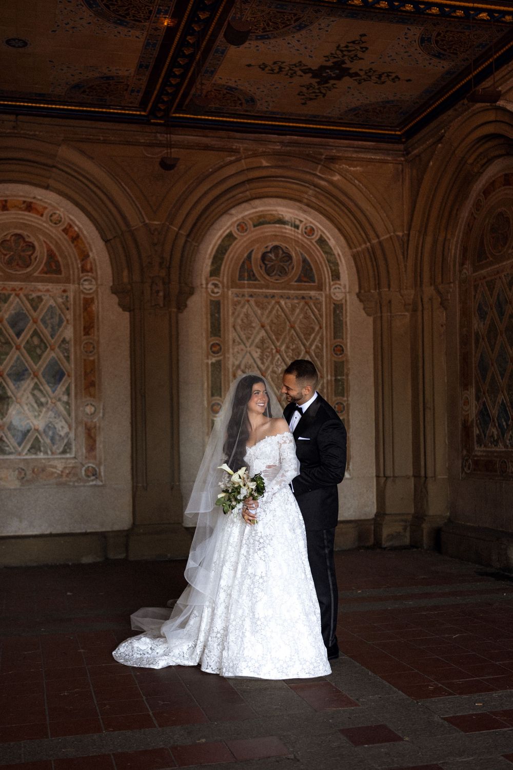A couple poses in an ornate architectural setting with decorative walls and arches.