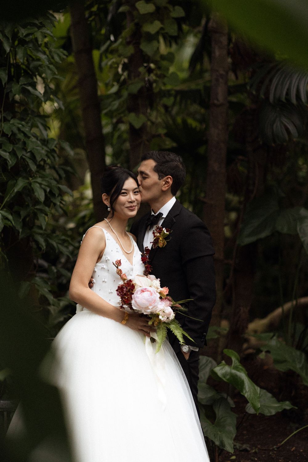 Romantic wedding couple embracing in a lush garden setting with white flowers.