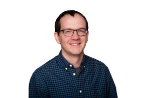 Professional headshot portrait of someone wearing glasses and a blue checkered shirt against a white background.