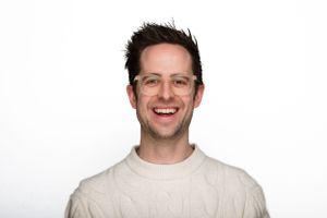 A smiling person wearing a cream colored sweater poses against a white background.