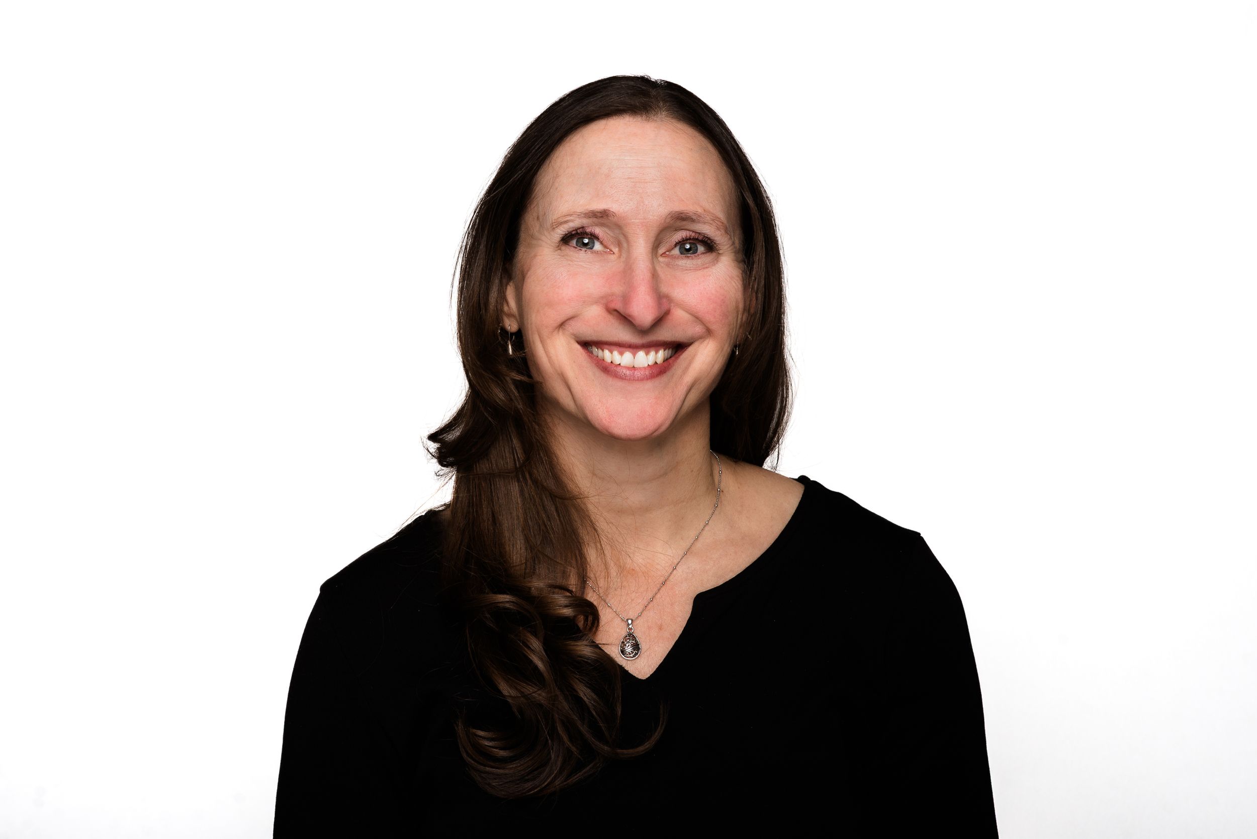 Professional headshot portrait of someone in a black sweater smiling against white background.