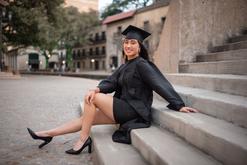 Dallas senior photo of stylish graduate in black dress smiling with cap and gown while sitting on staircase, Class of 2026