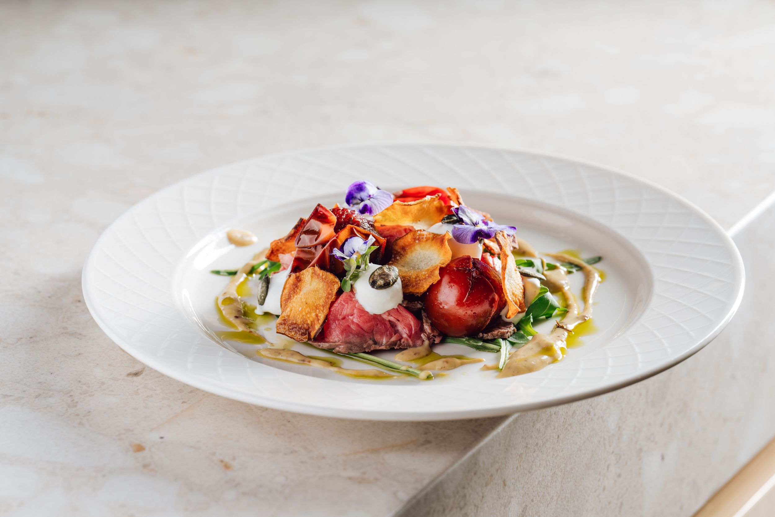 Artistically plated dishes with colorful garnishes and sauces on white porcelain plates.
