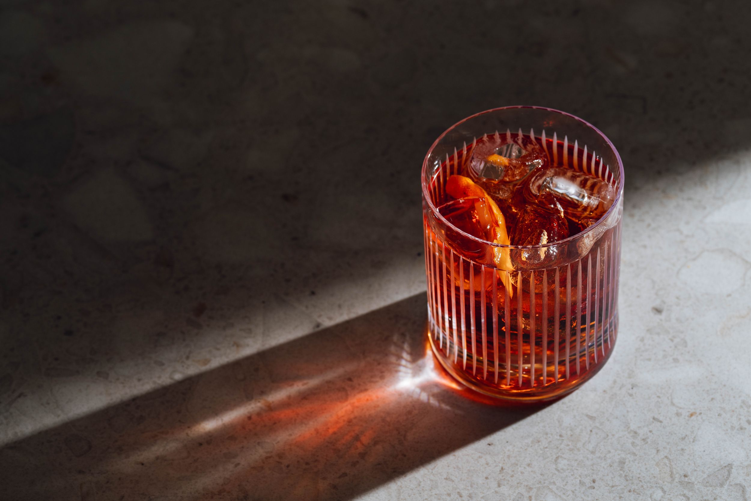 Illuminated cocktail glasses with orange lighting creating dramatic shadows and reflections.