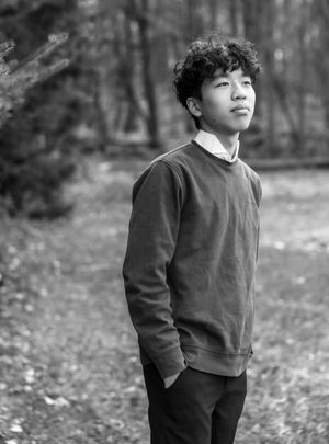 Black and white portrait series of a person in a dark sweater standing against a blurred forest background.