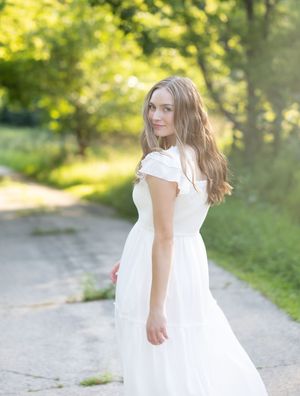 A child in a flowing white dress twirls playfully on a sunlit path surrounded by lush green foliage.