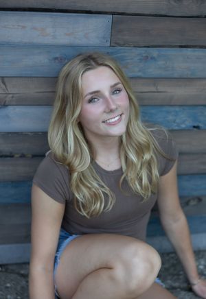 A person in a brown t-shirt poses against a rustic blue wooden wall background.
