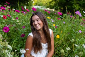 A person sits among vibrant pink and yellow cosmos flowers in a lush summer garden.