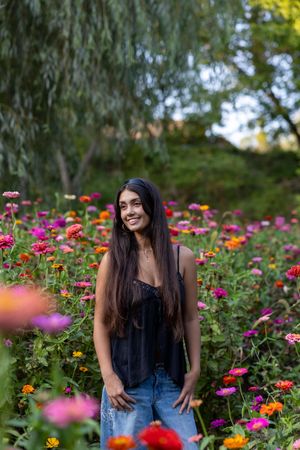 A person stands in a vibrant garden filled with colorful zinnias and wildflowers on a sunny summer day.