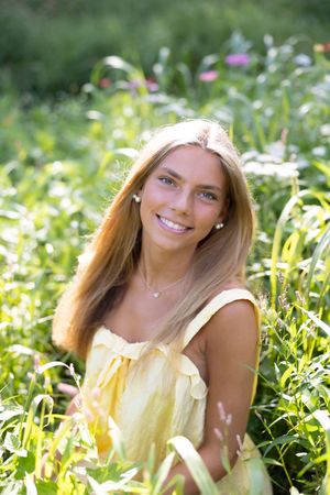 A person in a yellow sundress sits among wildflowers and greenery in bright summer sunlight.