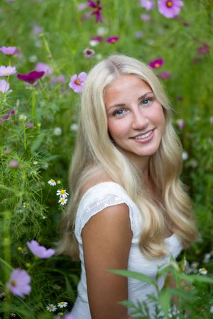 A person in a white dress poses among vibrant pink cosmos and white daisies in a summer garden setting.